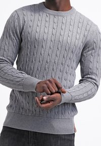 Pull gris en maille avec un motif torsadé, col rond, poignets et ourlet côtelés. Le tissu semble doux avec une finition texturée.