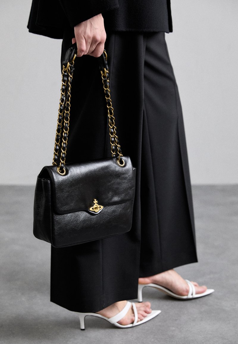 Bolsa de couro preta com um design estruturado, detalhes em metal dourado e uma alça de corrente. Possui uma aba frontal com um detalhe do logótipo.