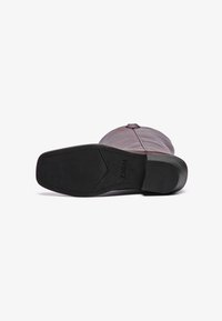 Botte en cuir marron avec une semelle en caoutchouc. Présente un design épuré, un bout arrondi et des coutures minimales. Logo du fabricant sur la semelle.
