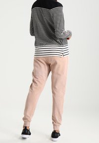 Top de manga larga a rayas blancas y negras con cuello negro, combinado con pantalones de chándal texturizados rosas claros y zapatillas negras.
