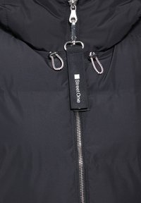 Giubbotto imbottito nero con colletto alto, zip argentata e un'etichetta di tessuto con la scritta "Street One". Presenta dettagli elasticizzati attorno al cappuccio e alla zip.