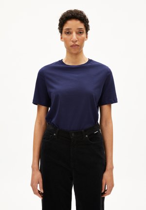 Dunkelblaues Baumwoll-T-Shirt mit Rundhalsausschnitt und kurzen Ärmeln, kombiniert mit hochgeschnittenen schwarzen Denim-Hosen. Einfaches Design, ohne Verzierungen.