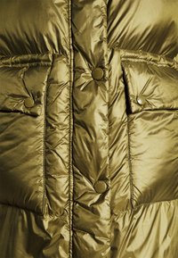 Giacca puffer verde oliva con tessuto lucido e raffinato. Presenta due tasche frontali con bottone e una chiusura con bottoni, oltre a una texture trapuntata.