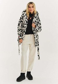 Polstrovaný kabát s černobílým květinovým vzorem a kapucí. Nositelný přes černý top, doplněný krémovými kalhotami a černými kotníkovými botami.