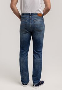 Niebieskie dżinsy z prostą nogawką, pięcioma kieszeniami oraz widocznymi detalami przeszyć. Talia ozdobiona jest brązową skórzaną naszywką z tyłu.