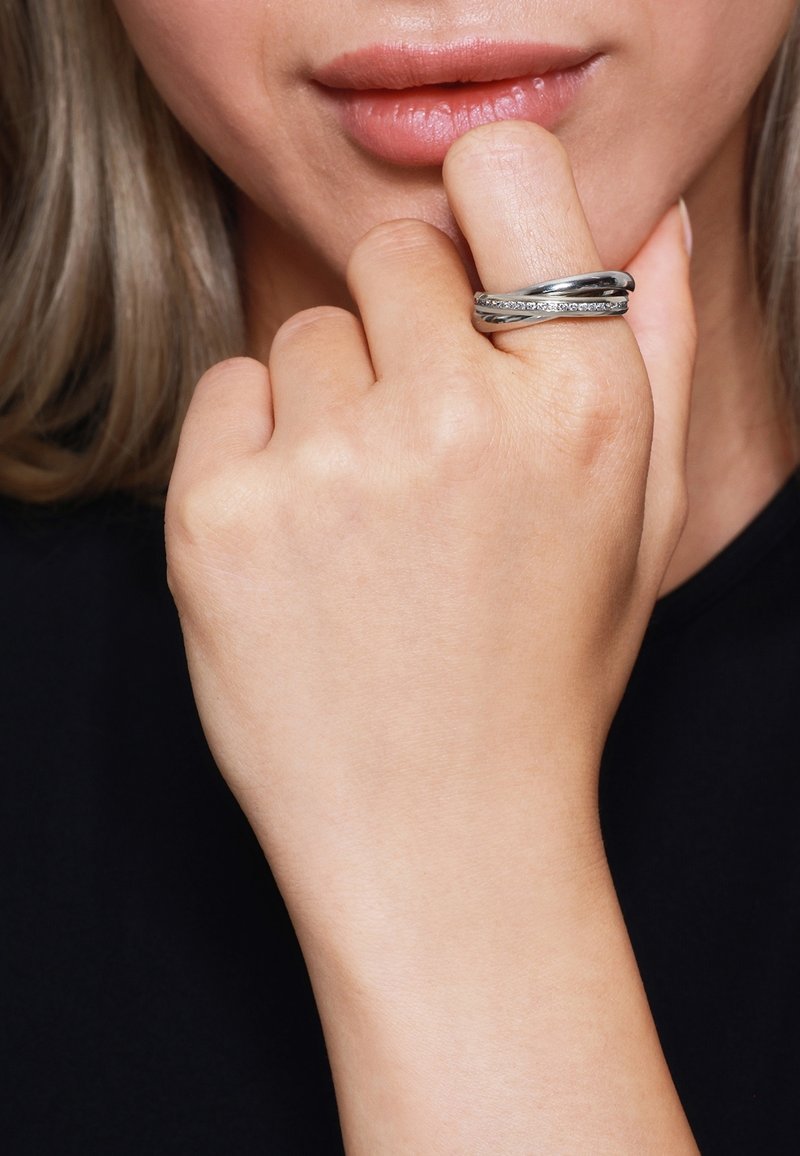 Gros plan d'une main touchant les lèvres avec une bague en argent ornée d'une rangée de petites pierres claires sur le majeur.