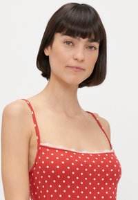 Red polka dot dress with thin straps, ribbed texture, and lace trim along the neckline. Features white, evenly spaced dots throughout.