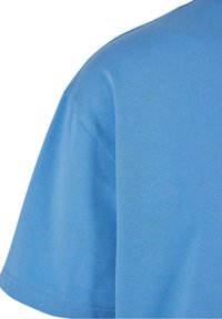 Gros plan sur une chemise en coton légère de couleur bleu clair à manches courtes, mettant en évidence la couture de l'épaule et la finition des manches.