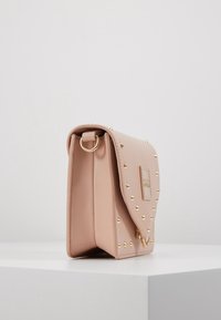 Pink leather handbag with gold studs, rectangular shape, flap closure, and a logo patch. The bag features a metal ring on the side.