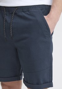 Mørkeblå shorts laget av lett materiale, med elastisk midje med snor, sidelommer og oppbrettede kanter.