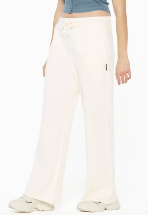 Cream-colored, wide-leg sweatpants made of soft fabric. Features elastic waistband with drawstring and side pockets. Accents include small logo.