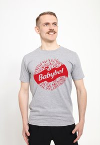 Šedé bavlněné tričko s velkým červeným logem "Babybel" a kruhovým designem malých červených kapek okolo něj. Krátké rukávy a kulatý výstřih.