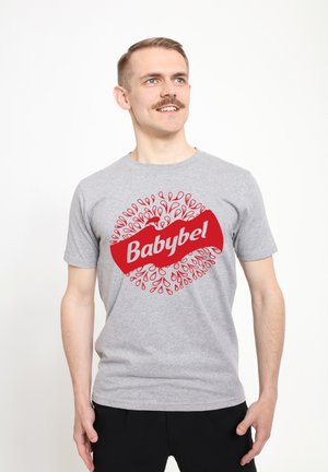 Šedé bavlněné tričko s velkým červeným logem "Babybel" a kruhovým designem malých červených kapek okolo něj. Krátké rukávy a kulatý výstřih.