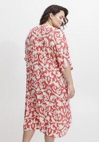 Lagani kimono do koljena u koraljnim i krem nijansama, s vrtložnim cvjetnim uzorkom i opuštenim rukavima, izrađen od prozračnog materijala.