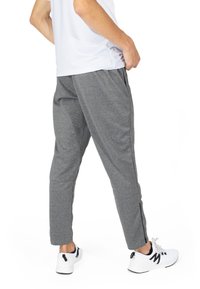 Šedé sportovní kalhoty s přiléhavým designem, se zúženými nohavicemi a bočními zipy, ve spojení s bílými teniskami a tričkem s krátkým rukávem.