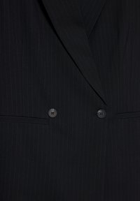 Sort blazer med stiklinger i striber, brede klapper, dobbeltbrystet design, to knapper og to vandrette forlommer.