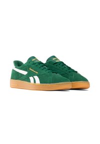 Chaussures de sport en suede vert avec des accents blancs, semelle en caoutchouc crème, et un détail logo doré sur la languette. Embout rond et design de laçage plat.