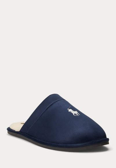 Παντόφλα σε ναυτικό μπλε, πάνω μέρος από απαλό ύφασμα, λευκό κεντημένο λογότυπο, στρογγυλή μύτη, επένδυση εσωτερικά αφράτη, ευέλικτη μαύρη σόλα, σχεδίαση για εύκολο φόρεμα.