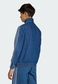 Giacca in denim blu scuro con collo alto, polsini elastici e strisce laterali. Presenta una vestibilità comoda e una texture liscia.