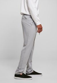 Helle graue Hose mit geradem Schnitt, elastischem Bund, seitlichen Taschen und subtiler Textur, kombiniert mit schwarzen Slippern.