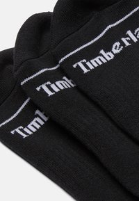 Calze nere con logo "Timberland" bianco, realizzate in tessuto morbido, con un polsino a costine e un design semplice e pulito.