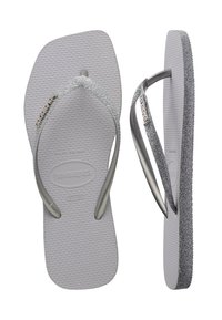 Tongs grises texturées avec des brides argentées pailletées, vues latérales et de dessus, montrant le logo Havaianas sur les brides et les semelles.