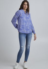 Lightweight blue shirt with a white dot pattern, button-down collar, and long sleeves, paired with distressed blue jeans and white sneakers.