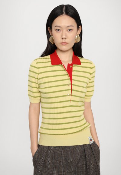 Knit polo-top dengan garis kuning dan hijau dan kerah merah, memiliki lengan pendek serta tombol di bagian depan, dipadukan dengan rok plaid.