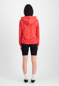 Sudadera con capucha roja, hecha de una tela suave, combinada con pantalones cortos de ciclismo negros. Incluye características como una gran capucha y puños acanalados.