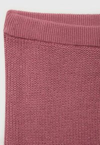 Vêtement tricoté en rose clair avec une surface côtelée et texturée et un large col plat. Le matériau semble doux et extensible.