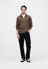 Suéter marrón con cremallera y cuello acanalado, combinado con pantalones negros y zapatos negros con acentos blancos. Diseño simple y moderno.