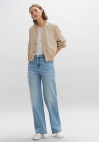 Beige windbreakerjas met een elastische tailleband, gecombineerd met lichtblauwe wijde jeans en witte sneakers. Eenvoudig, strak ontwerp en texturen.