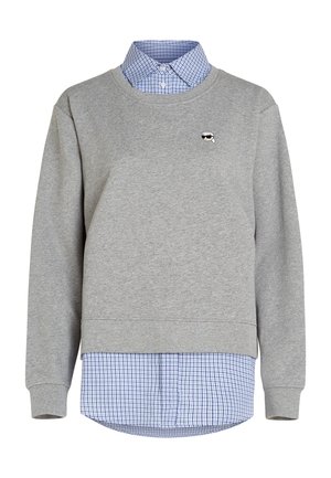 Szara bluza z okrągłym dekoltem założona na niebieską i białą koszulę w kratę z guzikami, z małym haftowanym logo na lewej piersi.