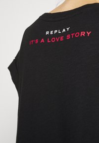 Černé tričko s krátkými rukávy. Na zadní straně se nachází bílé a červené vyšívané nápisy: "REPLAY, TO JE ROMANTICKÝ PŘÍBĚH." Měkká textilní struktura.