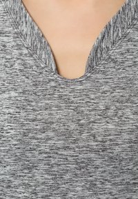 Top de tela gris texturizada con escote en V, que presenta un patrón sutil y mezclado. Material suave y liviano evidente en la vista de cerca.