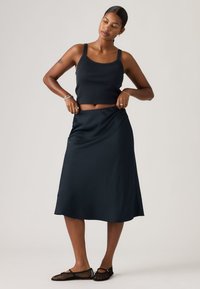 Débardeur noir raccourci et jupe longue sombre fluide, texture lisse, coupe décontractée, associé à des ballerines noires en maille. Design simple et élégant.