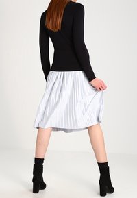 Czarna bluzka z długim rękawem w połączeniu z plisowaną, niebieską spódnicą do kolan. Całość dopełniają czarne botki za kostkę.