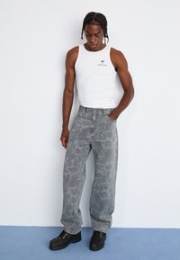 Grå camo-mønstrede højtaljede jeans, lavet af denim; parret med en hvid tanktop med et lille palme-logo og sorte snørebåndssko.