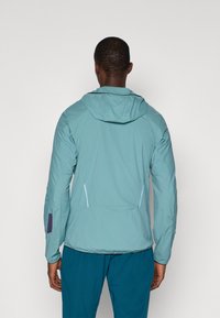 Ελαφρύ, τυρκουάζ μπουφάν με κουκούλα, πλαϊνές πάνελ και μωβ λεπτομέρεια στο μανίκι. Λείο υφή, εφαρμοστό σχέδιο και τσεπάκια με φερμουάρ.