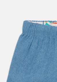 Lys blå denimstoff med elastisk midje og inner blomstertrykk. Viser den øverste delen og sømdetaljene av plagget.