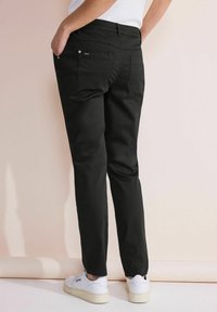 Svarta byxor med slim fit, tillverkade av bomull. Har två bakfickor och en jämn yta. Kombineras med vita sneakers.