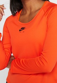 Nike longsleeve in fel oranje met een gestructureerde stof. Voorzien van een ronde halslijn en een zwart "Nike Air" logo op de borst.