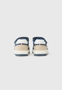 Marineblå og beige sneakers med borrelås, hvite detaljer, teksturert materiale og gummisåle med mønster.