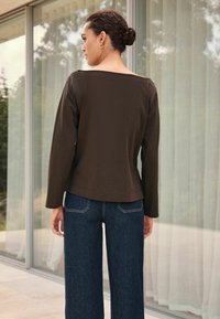 Brown long-sleeve top with a wide neckline, paired with high-waisted dark blue wide-leg jeans. Smooth fabric with a casual fit.