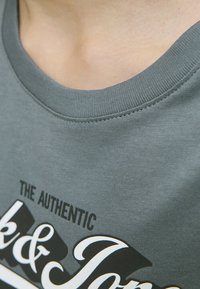 Camiseta de algodón gris con cuello redondo, que presenta un diseño de texto impreso en blanco y negro, textura suave y detalles de costura visibles.