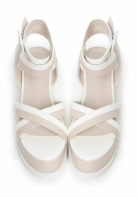 Sandalias de tiras en beige y blanco con suela plana, que cuentan con tiras cruzadas y una correa en el tobillo. Material sintético suave.
