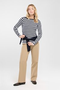 Mörkblå och vita randiga långärmade skjortor, beige vida byxor och svarta nätklackar. Skjortan bärs med en mörkblå knuten runt midjan.