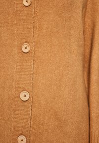Hnědý pletený svetr s pěti dřevěnými knoflíky a žebrovanou texturou podél předního zapínání. Měkká látka s teplým odstínem.