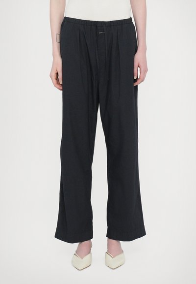 Pantalones negros de pierna ancha, hechos de una tela suave con una cinturilla elástica y pliegues frontales. Presentan un ajuste casual y relajado con dobladillos limpios.