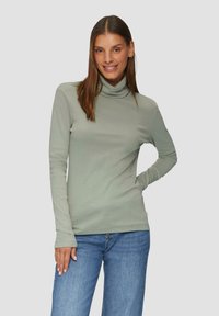 Jasnozielony golf z długim rękawem, wykonany z gładkiego materiału, w połączeniu z niebieskimi dżinsami. Charakteryzuje się dopasowanym krojem i wysokim dekoltem.